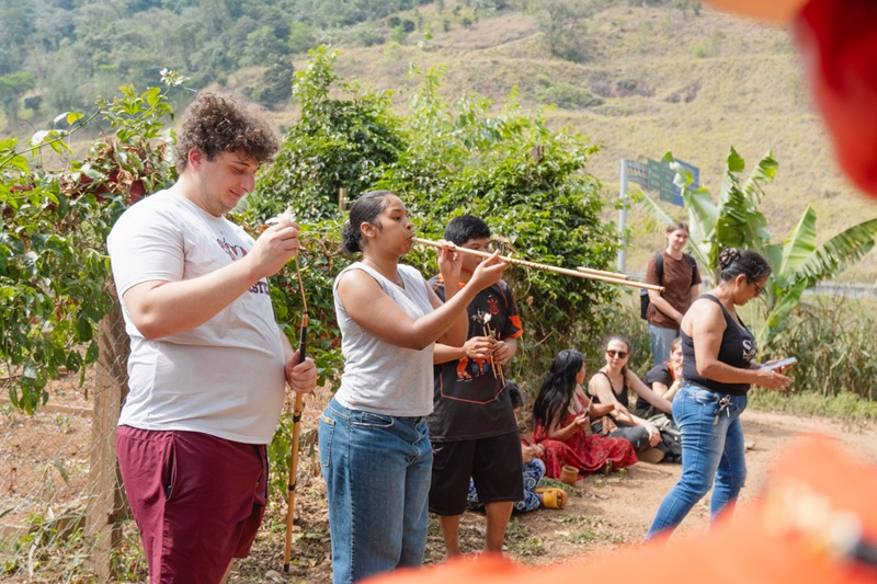 A CET Brazil student demonstrates how to use a traditional bamboo blowgun to a group of visitors outdoors.