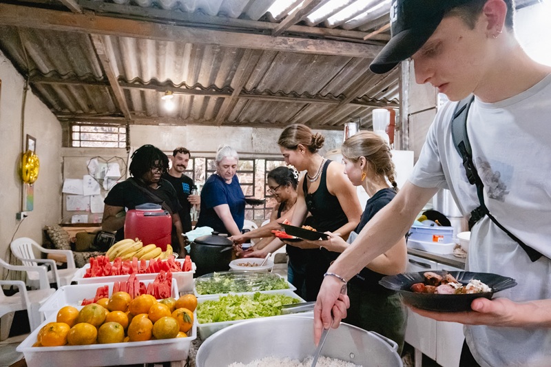 Students line up at a buffet inside a community kitchen filled with fresh fruit, salads, and rice.