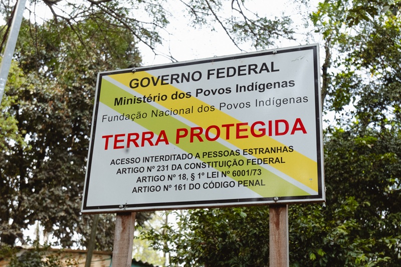 An official Brazilian federal sign reading "TERRA PROTEGIDA" (Protected Land) against a backdrop of green trees.