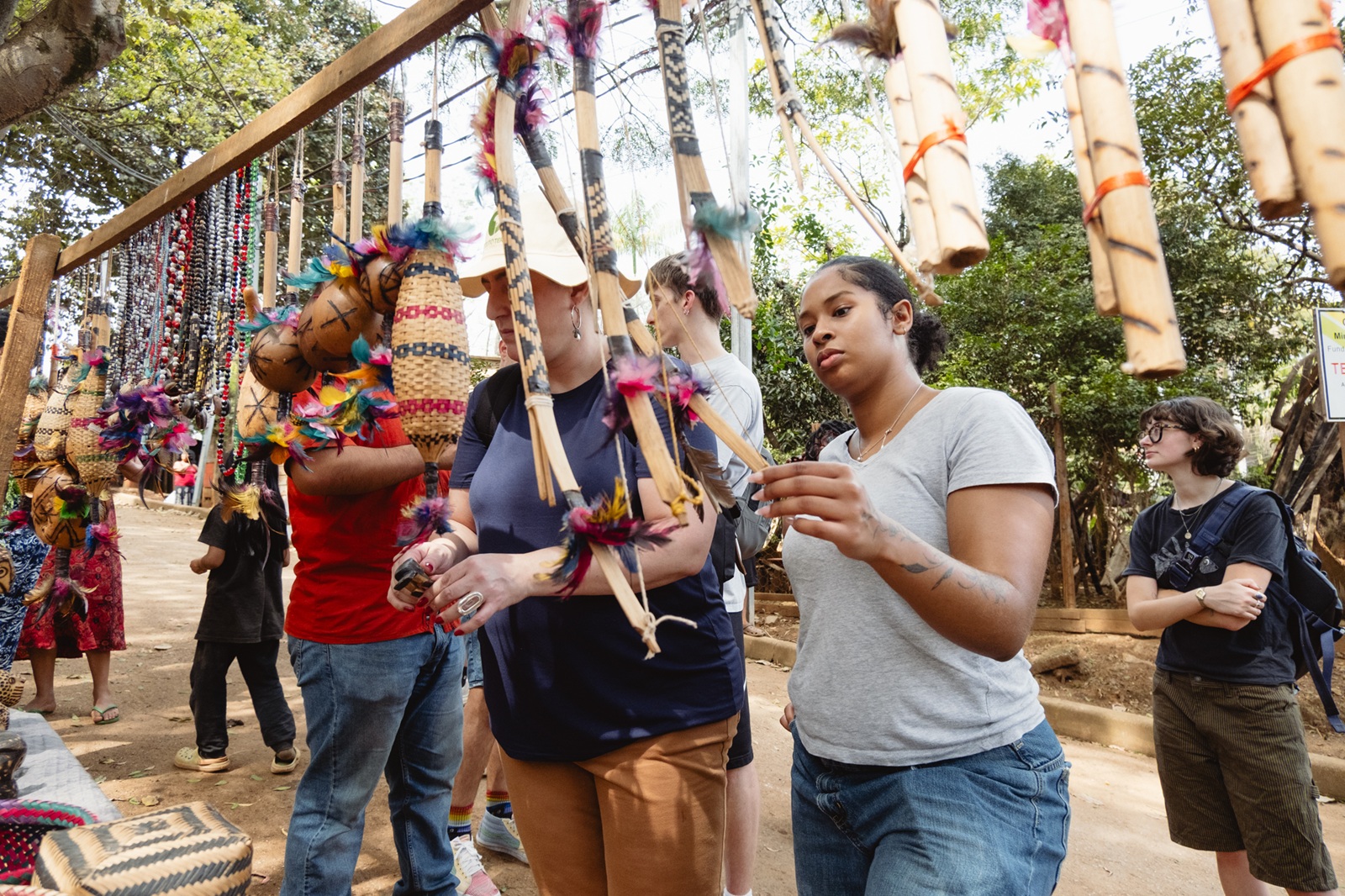 Visitors browse an outdoor market stall displaying handcrafted indigenous bows, arrows, and woven baskets.