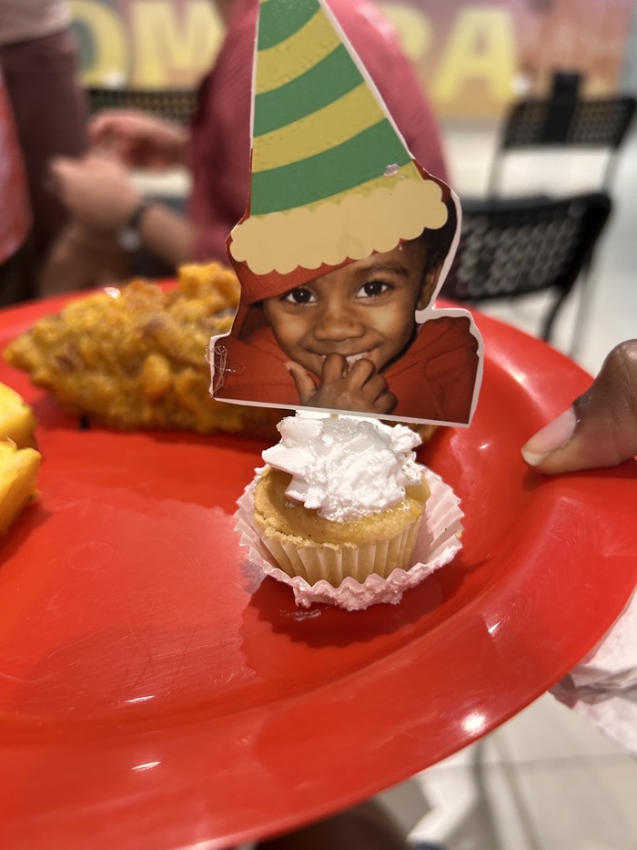 Cupcake topped with a baby photo decoration on a red plate.