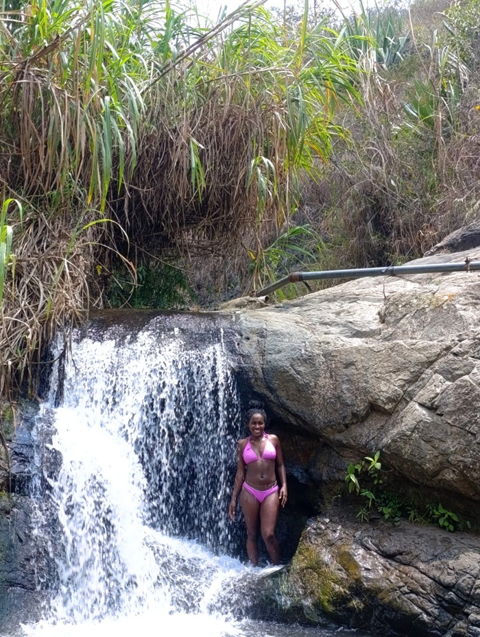 CET Colombia student standing beside a waterfall surrounded by rocks and greenery.