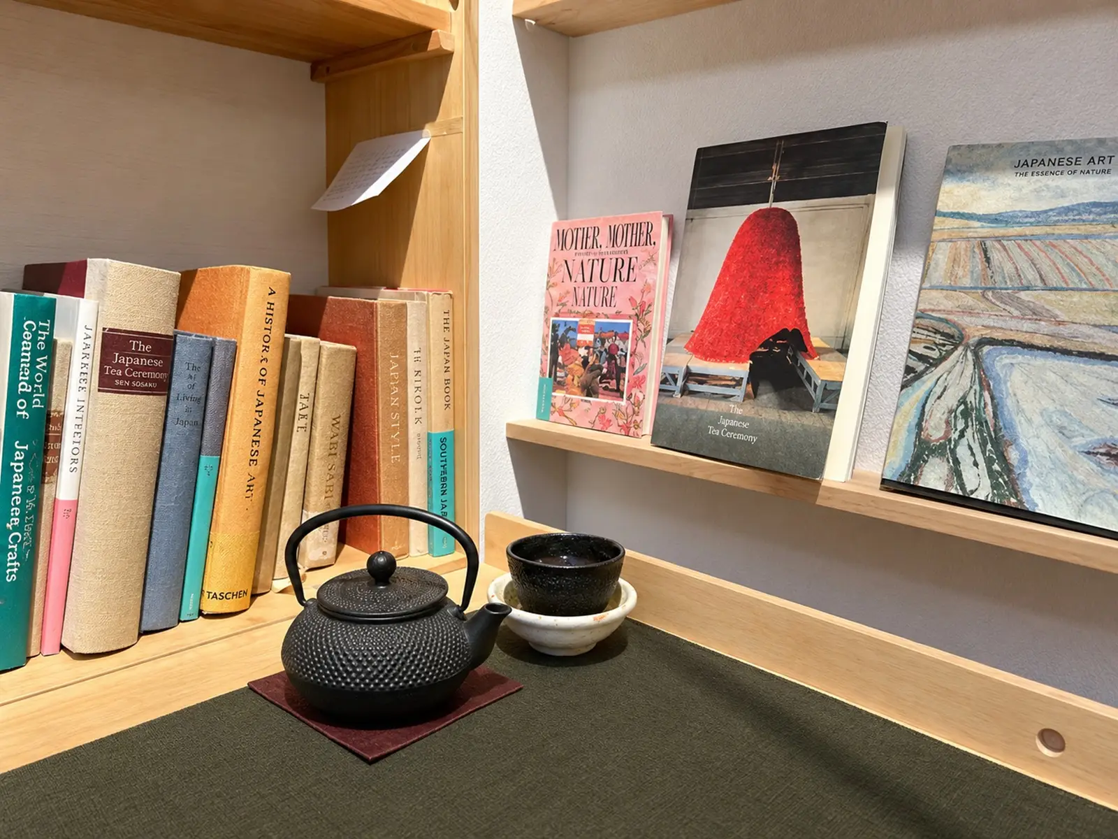 A small tea pot with a cup besides books on a shelf