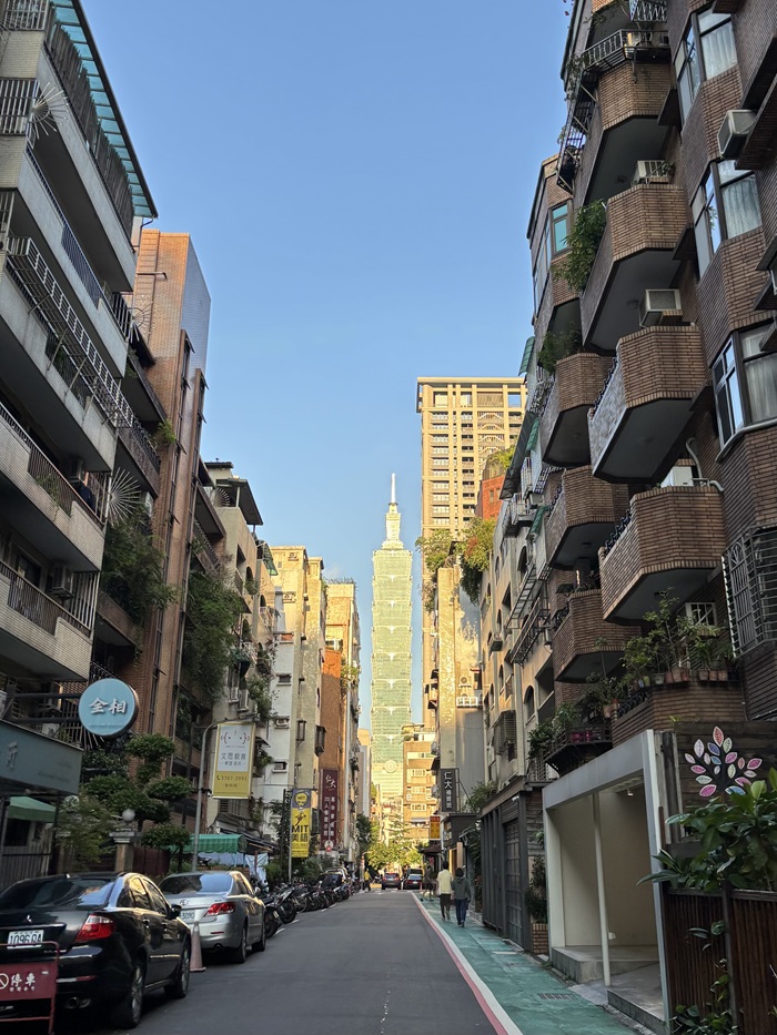 A classic street-level view looking down a narrow urban alleyway straight toward the Taipei 101 skyscraper in Taiwan.